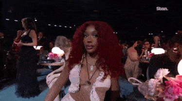 a woman with red hair is sitting in a very revealing dress in a crowded room .