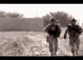 two soldiers are walking through a field with guns .