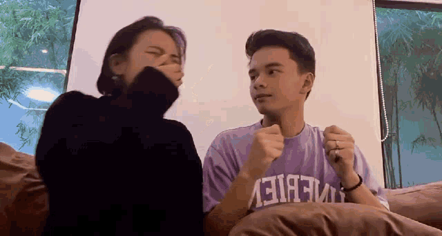 a man wearing a purple t-shirt with the word believe on it is sitting next to a woman on a couch