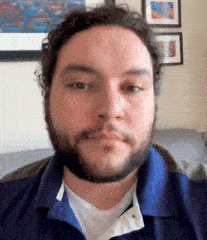 a man with a beard wearing a blue shirt is sitting on a couch