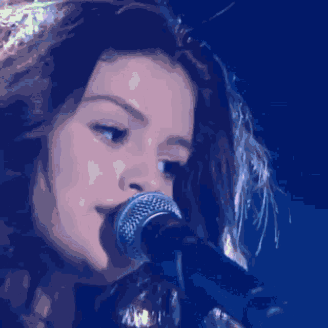 a woman singing into a microphone in a blue background