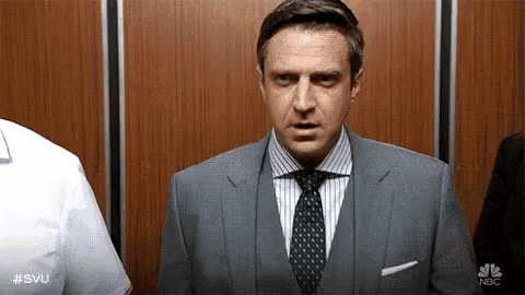 a man in a suit and tie is standing in an elevator looking at the camera .