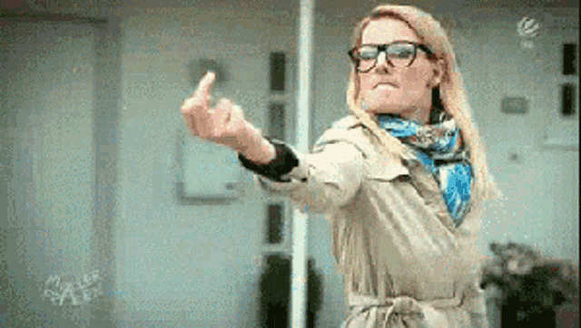 a woman in a trench coat and glasses is giving the middle finger