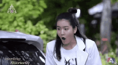 a woman is standing next to a car with her mouth open and a surprised look on her face .