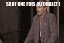 a man in a suit stands in front of a sign that says sauf une fois au chalet