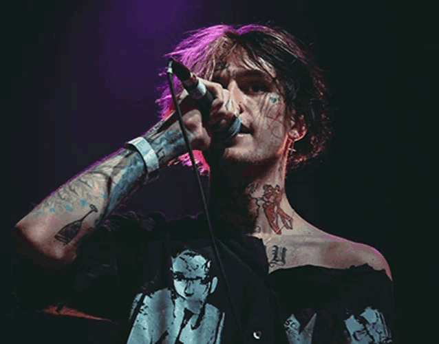 a man singing into a microphone with tattoos on his arms and neck