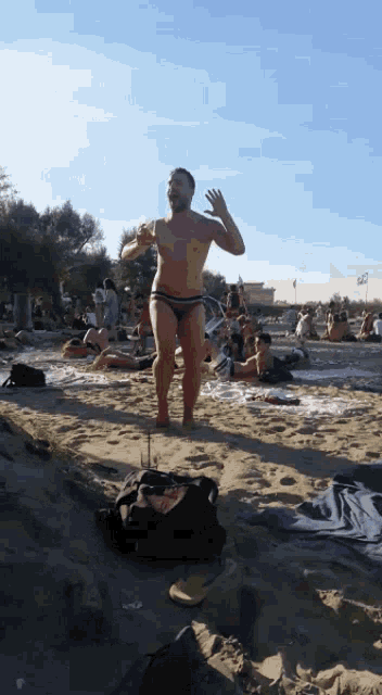 a man in a bikini stands on a sandy beach holding a drink