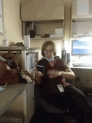 a woman wearing glasses and a mask sits at a desk in front of a computer