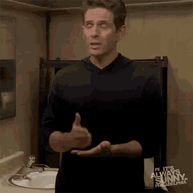 a man is standing in front of a sink in a bathroom giving a thumbs up .