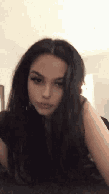 a woman with long black hair is sitting on a bed in a room .