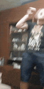 a man in a black shirt and blue shorts is dancing in front of a wooden wall .
