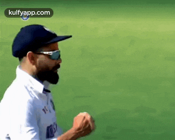 a bearded man wearing sunglasses and a hat is running on a green field .