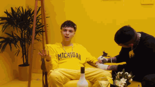 a man wearing a yellow michigan shirt is getting a tattoo