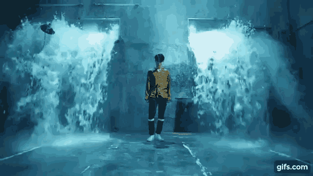 a man in a yellow jacket is standing in the middle of a waterfall .