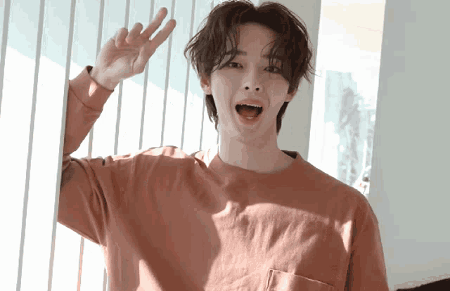 a young man wearing a pink shirt is waving his hand