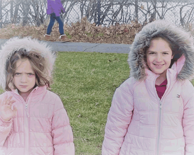 two girls wearing pink jackets with fur hoods are standing next to each other