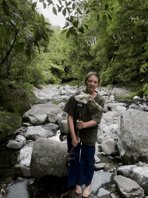 a person standing in a stream holding a stick that says ' abercrombie & fitch ' on the front