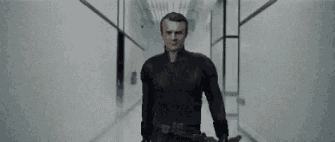 a man in a black suit is standing in a hallway next to another man