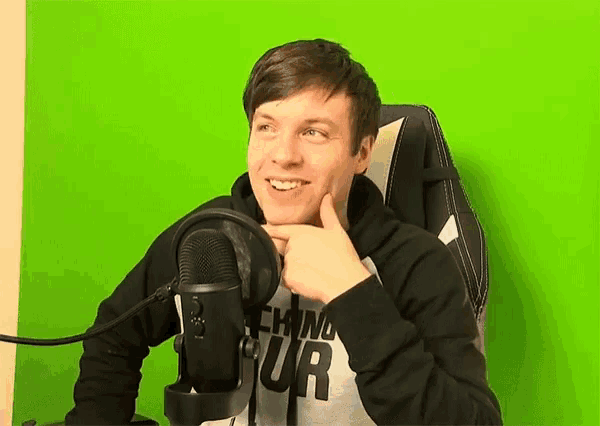a young man wearing headphones and a shirt that says techno tour is sitting in front of a green screen
