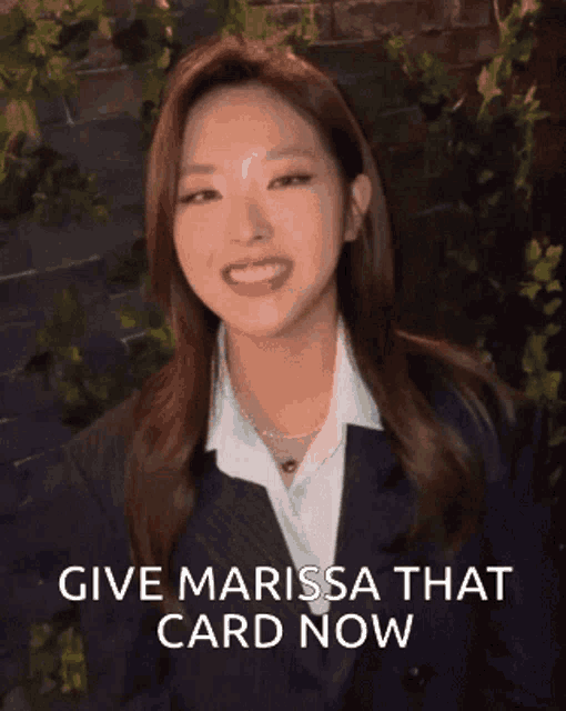 a woman in a suit and white shirt is smiling and says " give marissa that card now "