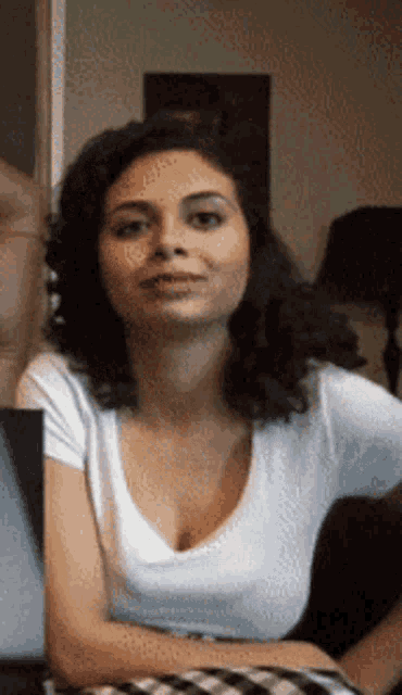 a woman in a white shirt is sitting on a couch and smiling