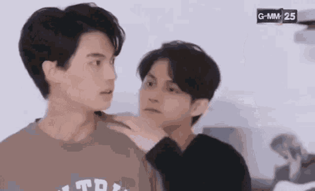 two young men are standing next to each other in a room and one of them is touching the other 's neck .