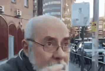 a man with glasses and a beard is drinking a glass of water on a city street .