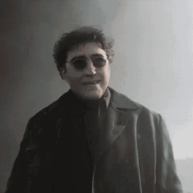 a man in a black coat and sunglasses is smiling