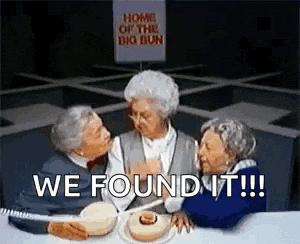three elderly women are sitting at a table with a sign that says `` home of the big bun '' behind them .