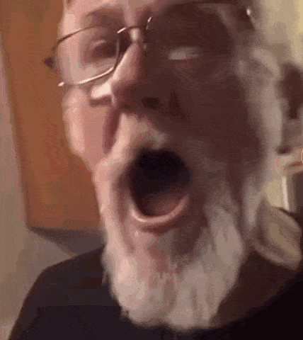 an older man with a beard and glasses is yawning .