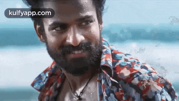 a man with a beard wearing a colorful shirt is standing on the beach .