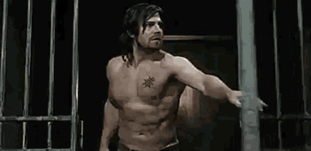 a shirtless man is standing in front of a fence in a dark room .