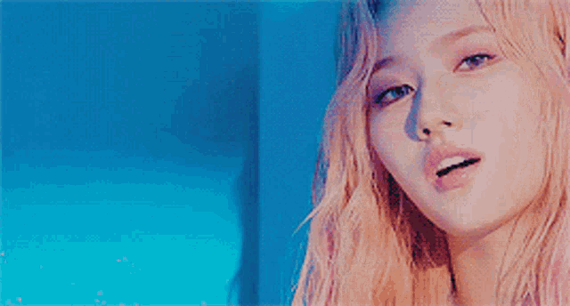 a close up of a woman 's face with pink hair against a blue background