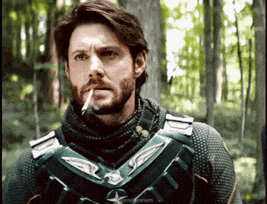 a man with a beard is smoking a cigarette in the woods and the caption says " enslaveham "