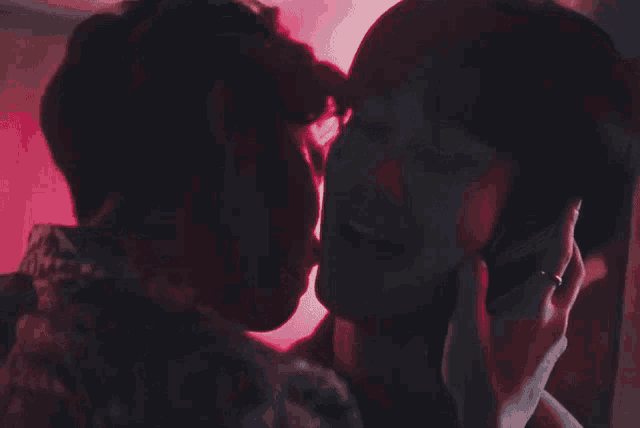 a couple kissing in a dark room with a red light behind them