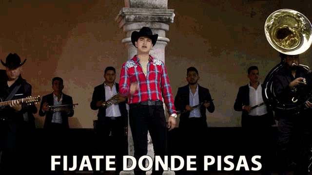 a man in a cowboy hat stands in front of a band with the words fijate donde pisas written below him