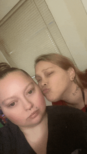 a woman with a tattoo on her neck is kissing another woman 's cheek