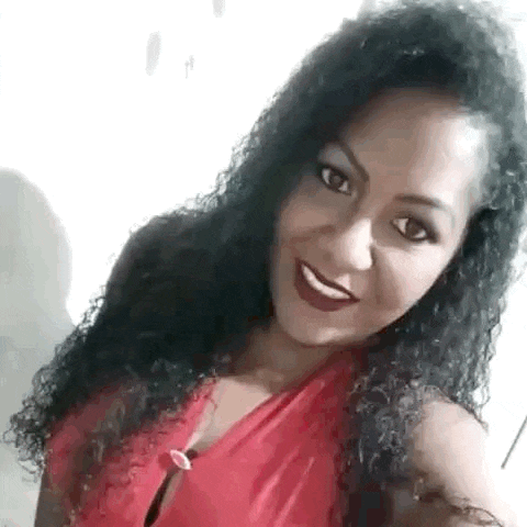 a woman with curly hair is wearing a red top and smiling .