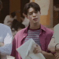 a man in a pink shirt is holding a piece of paper and looking at it .