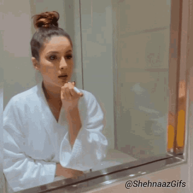a woman in a bathrobe is applying lipstick in front of a mirror with the hashtag @sehnaazgifs