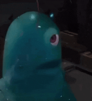 a blue monster with a red eye is sitting on a table in a dark room .