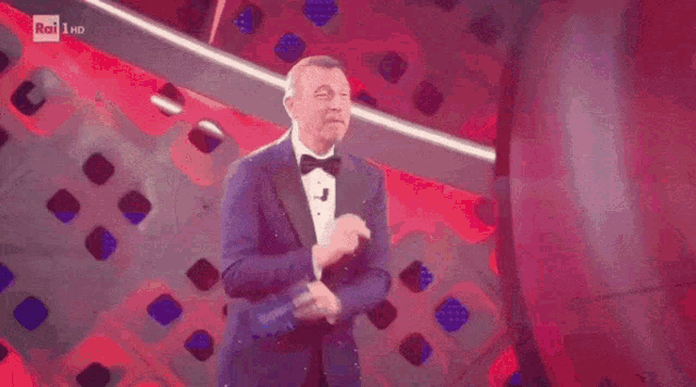 a man in a tuxedo and bow tie is dancing in front of a red background with rai hd written on it