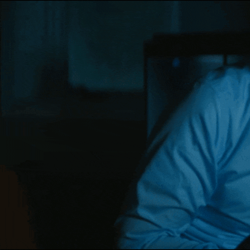 a person in a blue shirt is sitting in a dark room