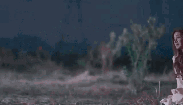a woman is sitting on the ground in a field at night with a ghost in the background .