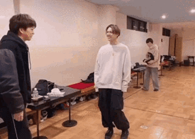 a man in a white sweater is standing in a room talking to another man .