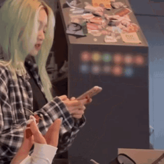 a woman with green hair is holding a cell phone in her hands .