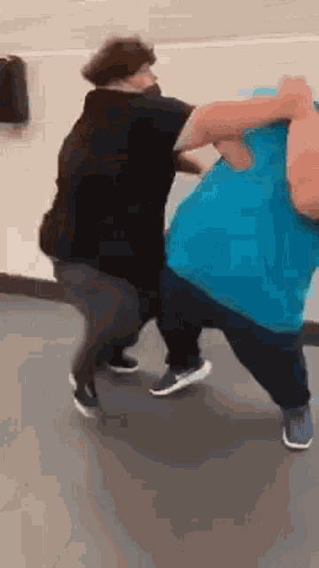 two people are fighting in a gym and one is wearing a blue shirt .