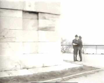 a man in a hat stands in front of a brick wall .