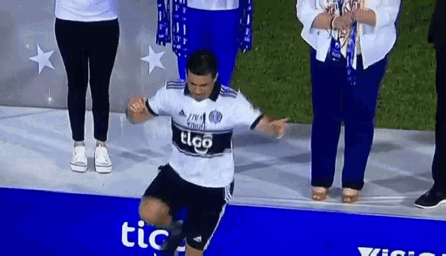 a man wearing a tico jersey is kneeling down on a stage