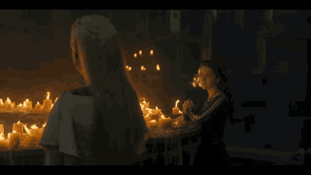 two women standing next to each other in front of a row of lit candles